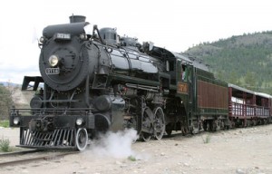 The historic 3716 steam locomotive blowing steam as it pulls passenger cars along the scenic tracks of the Kettle Valley Railway